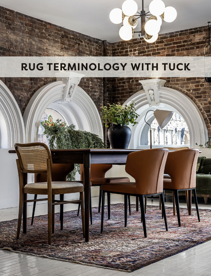 Dinning room with wood table, wood and rattan chairs, brick walls, and round historic windows with a vintage rug