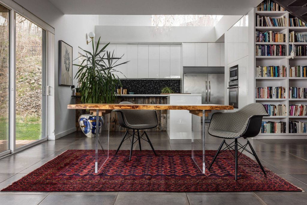 Dining room with wood slab table, red vintage rug, and floor to ceiling bookshelves in the background.
