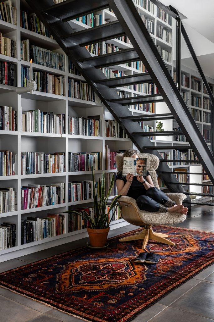 Bookshelves with red vintage carpet and women reading on a chair.