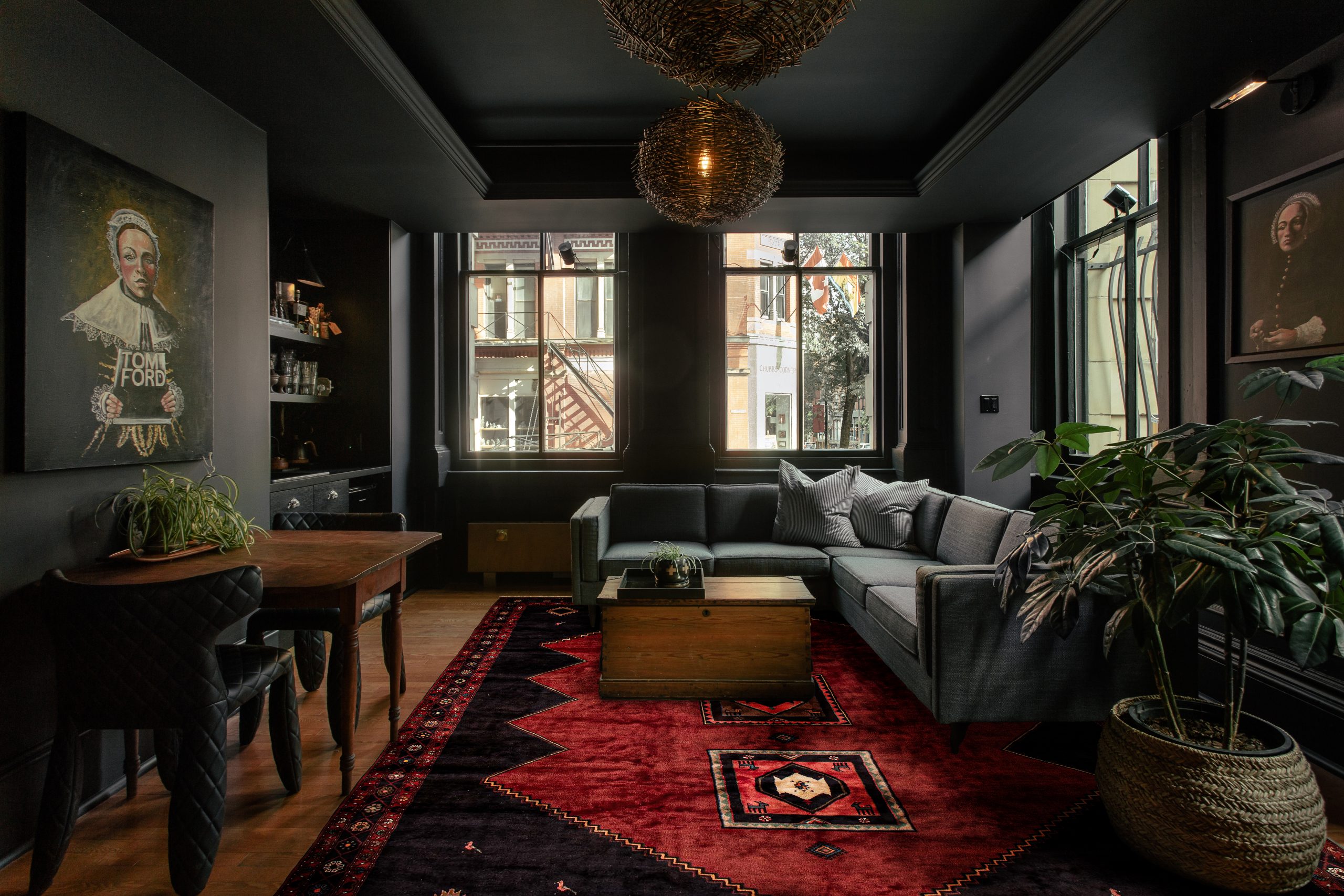 Living room with dark walls, gray sectional sofa, and a red geometric Tuck Rug featuring black accents and tribal patterns, adding warmth and contrast to the modern decor.